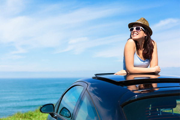 A photo of a woman who would benefit from car insurance, smiling while leaning on the top of her car through the sunroof