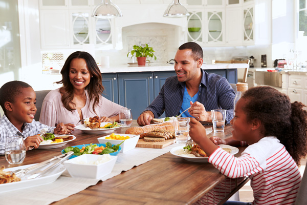 A happy family of four eating dinner in their house, protected with home insurance