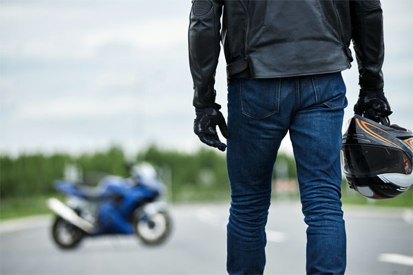 Photo of a man standing in front of his motorcycle, which would benefit from motorcycle insurance