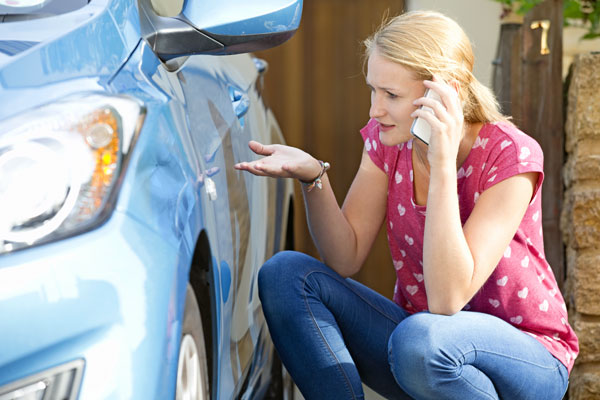 Photo of a woman inspecting car damage