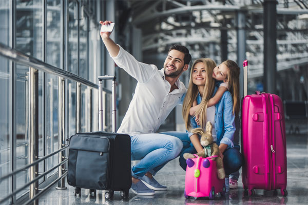 A photo of a family taking a selfie at the airport with their luggage